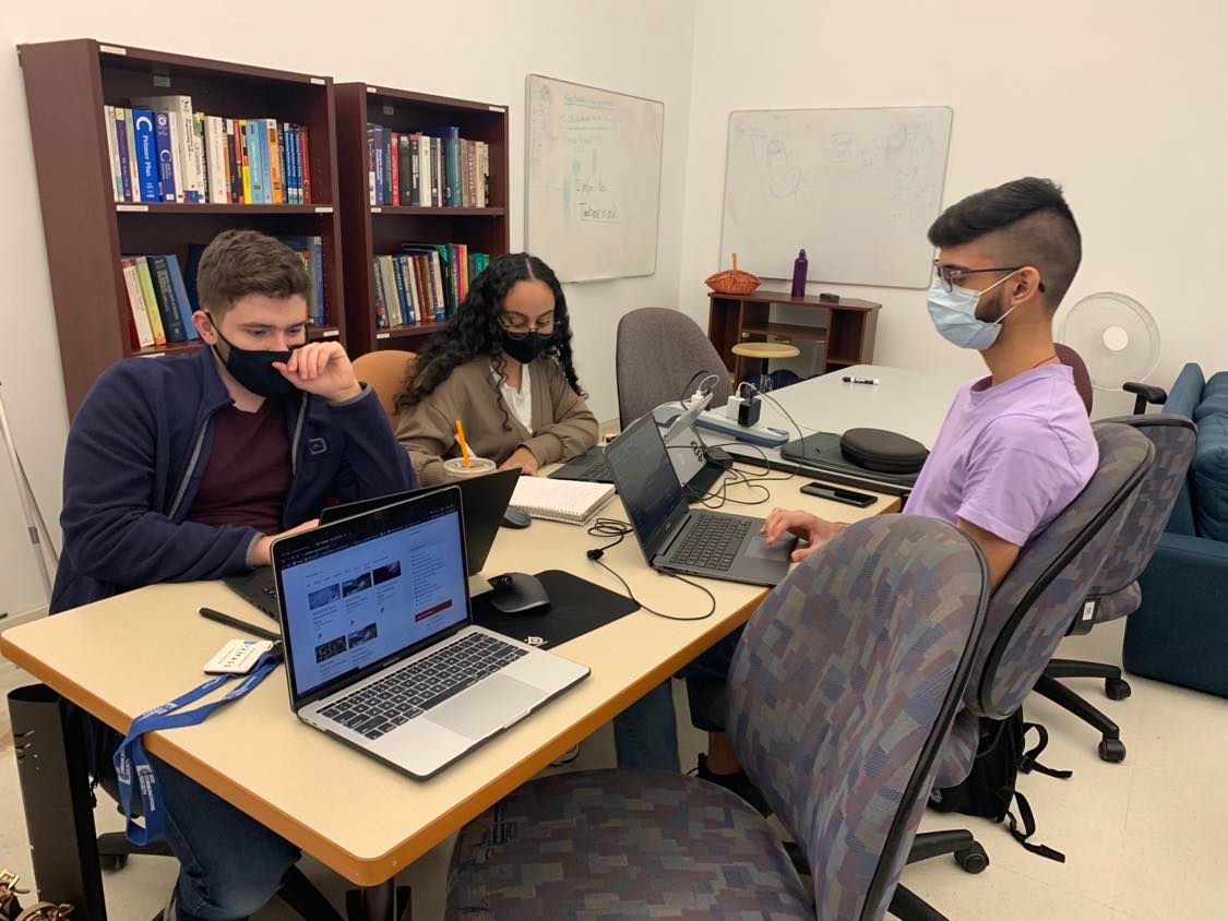 Picture showing 3 students with laptops and notebooks focused on school work